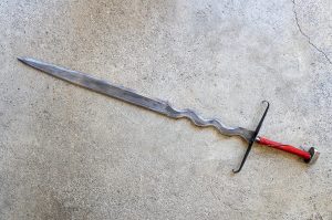Metal sword sculpture with wavy blade and red leather wrapped handle