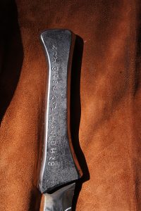 Handmade steel knife handle with Dune engravings on it laying on draped leather